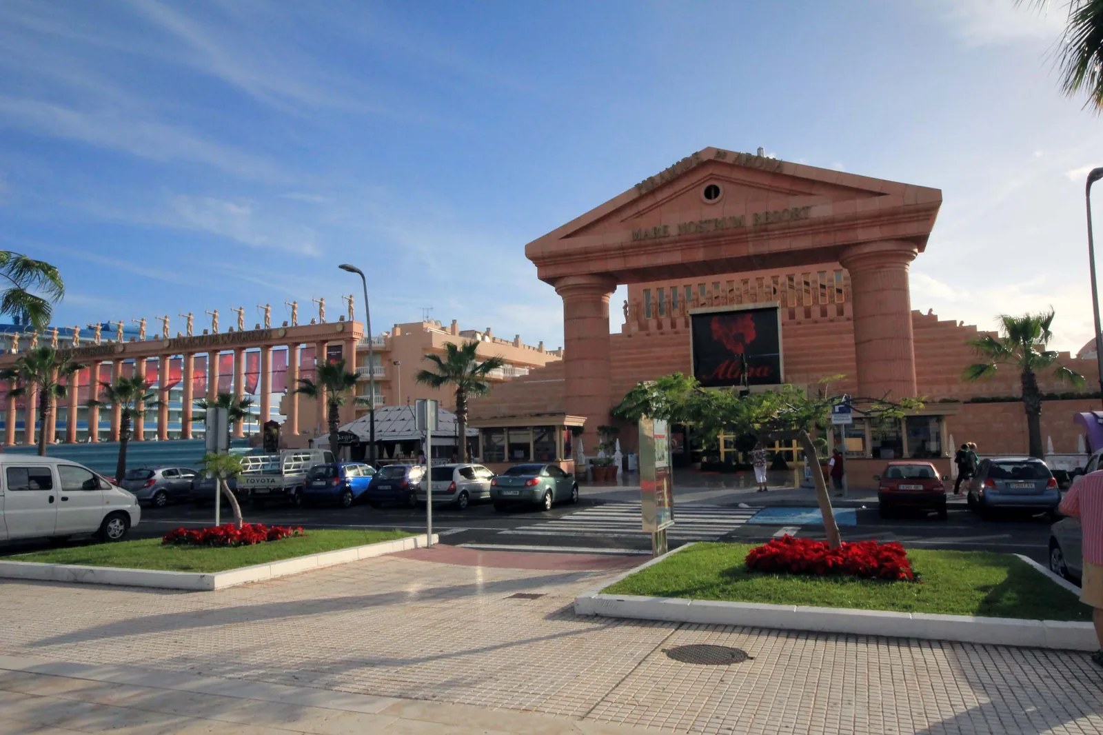 The pink stone entrance gate of the Mare Nostrum Resort on Avenida de las Américas, a pediment on two tall columns, with palm trees and a pedestrian crossing in front